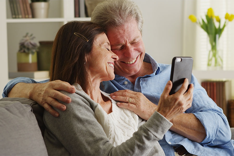 Client Center - Portrait of Smiling Mature Couple Spending Time Together on the Sofa and Using a Cellphone