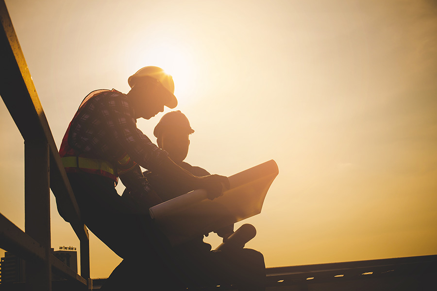 Specialized Business Insurance - Silhouette of Engineer and Contractor Discussing Building Plans While Sitting on a Construction Jobsite at Sunset